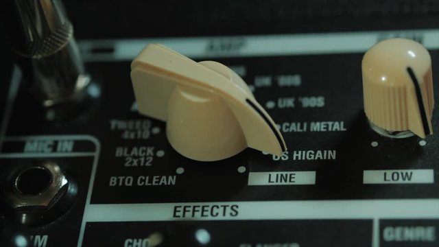 Men's hands twist tumblers on control panel of guitar amplifier. A mode switch being switches on amp. Man's hand inserts cable jack in guitar amp