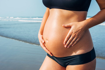 Fototapeta na wymiar Close up of pregnant woman belly wearing black bikini on the sea background