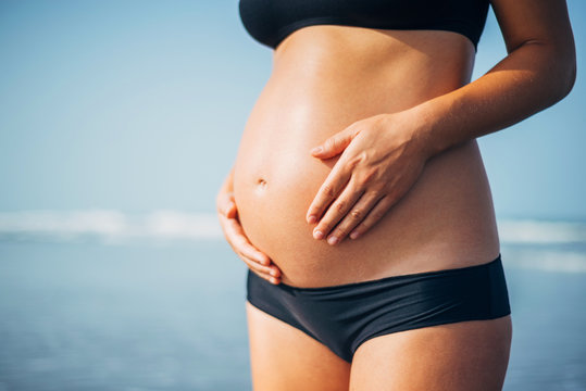 Close Up Of Pregnant Woman Belly Wearing Black Bikini On The Sea Background