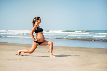 Fototapeta na wymiar Pregnant woman on the beach doing yoga. Pregnant woman doing workout near the the sea.