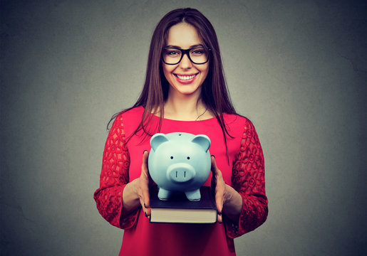 Student, happy woman, holding books and piggy bank in hands