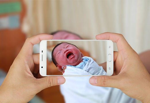 Hands taking picture of Newborn baby with smartphone.