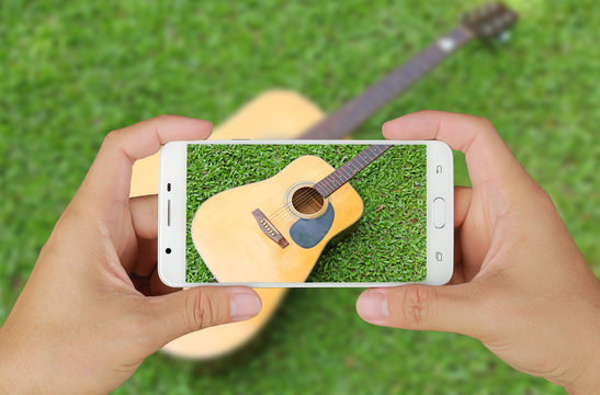 Hands taking picture of guitar on green grass with smartphone.