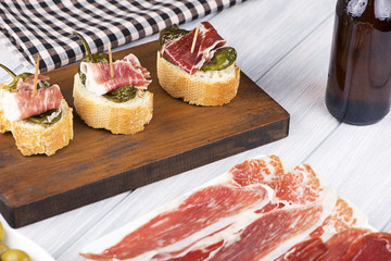 Appetizer of Iberian ham and green peppers next to Iberian ham dish and a beer. Spanish food.