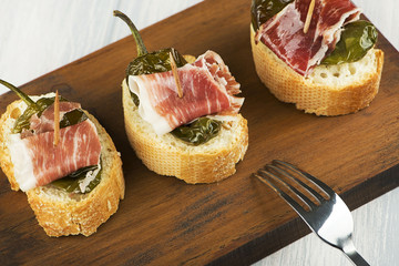 Close-up of Spanish tapas of ham and green pepper next to a fork on wooden board. Spanish gastronomy. Food.