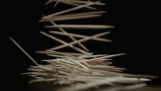 Slow motion. A lot of toothpicks fall down horizontally on a table black background