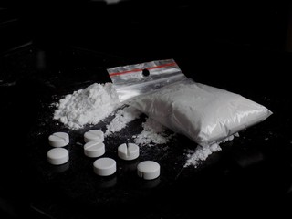 Cocaine drug powder bag and pile and pills on black background