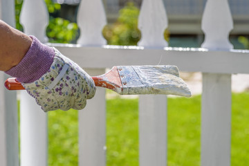 woman holding paintbrush in front of white picket fence on sunny day