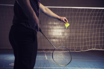 Man going to throw shuttlecock over the badminton net. Pitch. Indoors. Dark dim light. Toned image