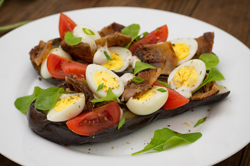 Baked eggplant with bacon, garlic and quail eggs. Wooden background. Top view. Close-up