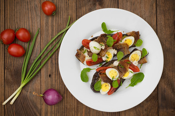 Baked eggplant with bacon, garlic and quail eggs. Wooden background. Top view. Close-up