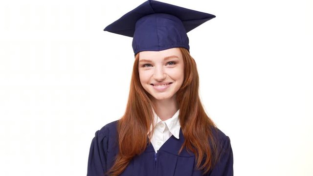 Beautiful young ginger Caucasian girl laughing at camera on white background wearing blue robe and square academical cap
