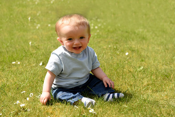 Happy ten month old baby boy sitting down outdoors on a sunny day 