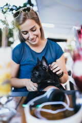 Beautiful young woman sitting in cafe with her adorable French bulldog puppy. Spring or summer city outdoors. People with dogs theme.