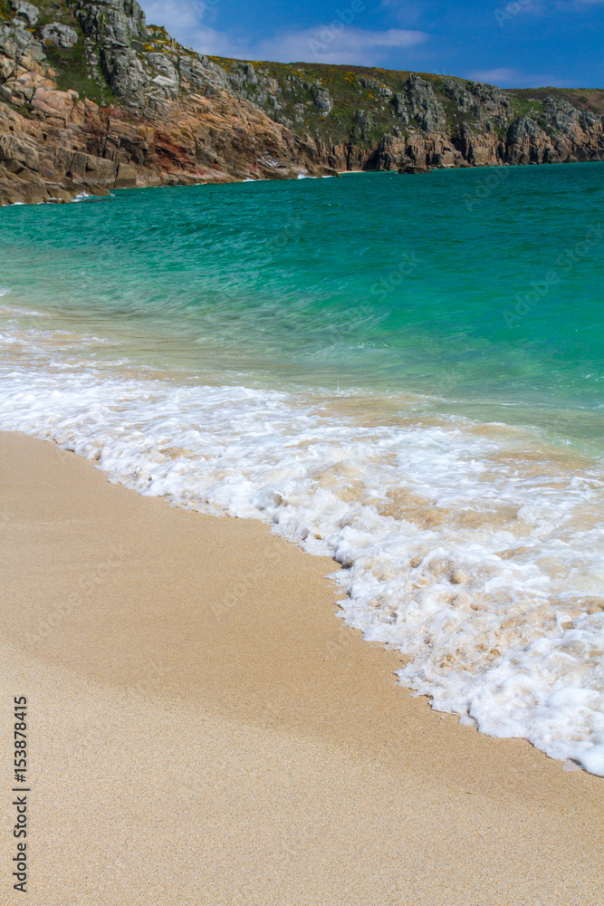 Wall mural the sandy beach and emerald green ocean off porthcurno beach in cornwall, uk with cliffs in the back