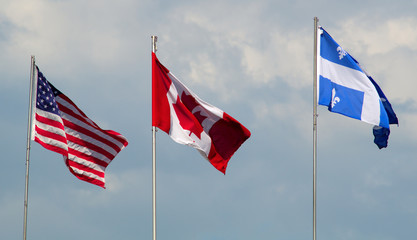 Canada, USA, and Quebec flags waving in the wind cloudy day