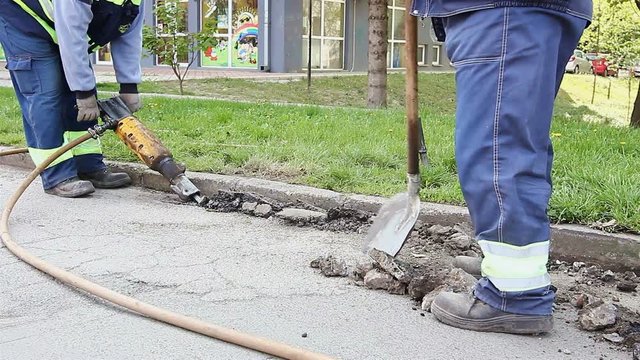 Worker with a shovel collects broken asphalt behind jackhammer
Labor with a shovel collects broken asphalt after another construction worker is using jackhammer.
