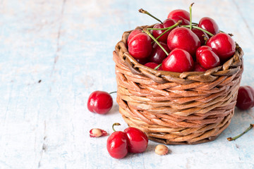 
 Fresh berries. Red ripe cherry in a round wicker basket on a light wooden background.