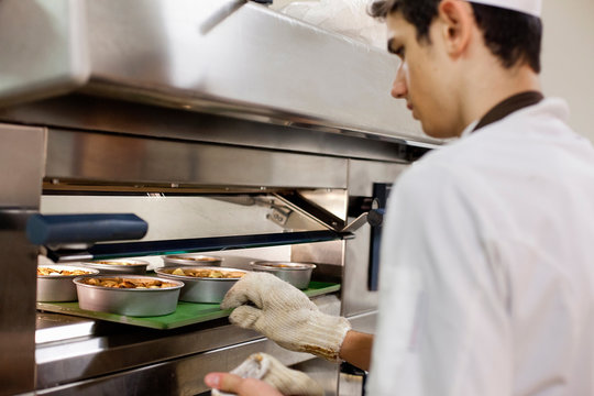 Baker putting food in oven in kitchen