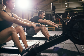 Sportsmen doing exercises with?rowing machine together - Powered by Adobe