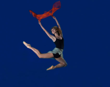 Young female dancer jumping mid air with red scarf
