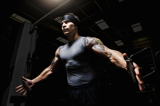 Muscular young man performing pulldown exercises in gym