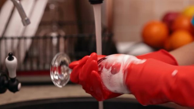 Closeup of hands in rubber gloves washing and rinsing a glass at the kitchen sink - camera slowly tilts down
