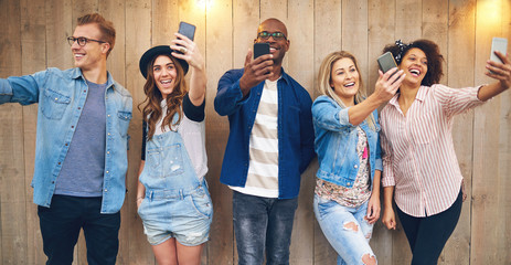Happy multiethnic friends taking selfie at wooden wall