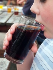 Young man drinking a cola type soft drink from a glass at an outside table at a public house in the UK.