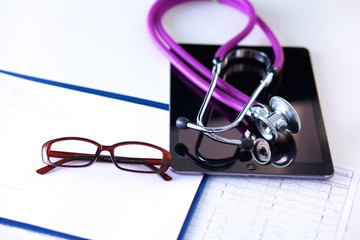 Tablet computer with a stethoscope lie on a table