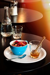 Breakfast in restaurant, oatmeal with strawberries in a blue cup with honey jar. Sunlight effect