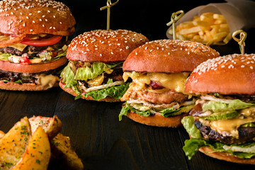Assorted burgers with different fillings, with sesame seeds on wooden table isolated on black background.