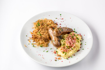 Grilled sausages, potatoes and braised cabbage on white plate close-up view from above.