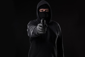 Masked robber with gun aiming into the camera against a black background