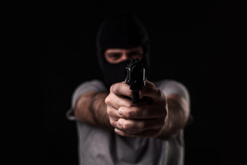 Naklejka premium Masked robber with gun aiming into the camera against a black background