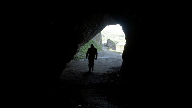 A silhouette of a person walking into a dark cave