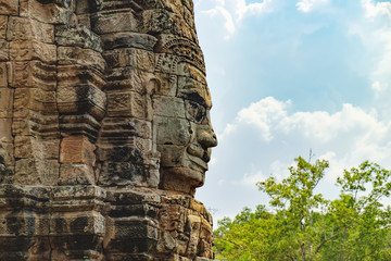 Smiling stone face of Prasat Bayon, the central temple of Angkor Thom Complex, Siem Reap, Cambodia. Ancient Khmer temple is surrounded by tropical trees, famous Cambodian landmark, World Heritage.