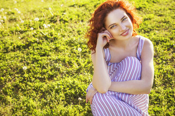 Naklejka na ściany i meble Beautiful red haired woman with fresh flawless skin and curly hairstyle in dress and a hat, smiling cheerfully in park. ideal teeth. Sunny day