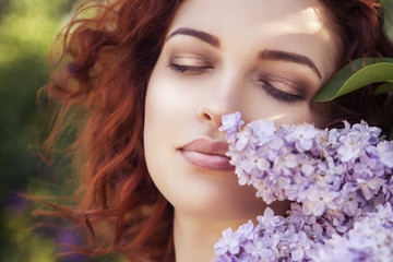 Naklejka premium Beautiful red haired woman with fresh flawless skin and curly hairstyle in dress in park near flowers. Sensual, sexy, soft emotion. Sunny day
