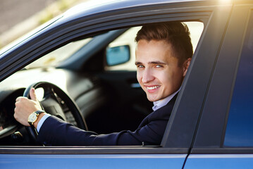 Attractive handsome smiling man in a business suit driving an expensive car