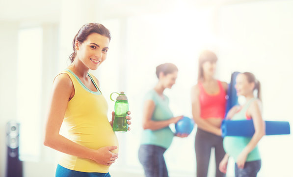 happy pregnant woman with water bottle in gym