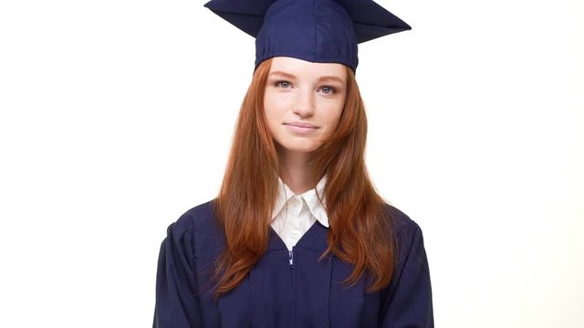 Beautiful young giger Caucasian girl laughing at camera on white background wearing blue robe and square academical cap in slowmotion