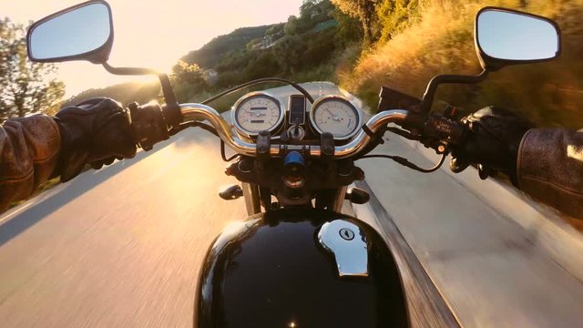 POV of masculine and manly motorcycle driver driving his vehicle through the windy mountain empty road in beautiful scenery on summer day full of thrilling adventures, with light leaks and flares