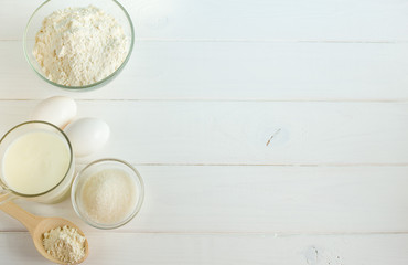Cooking bread in the kitchen from the ingredients: flour, sugar, salt, eggs. Roller, wooden spoons, corolla on a white wooden background