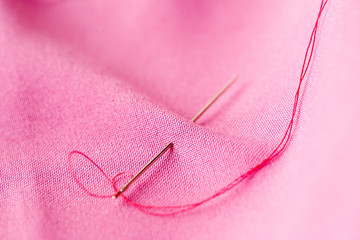 sewing needle with thread stuck into pink fabric