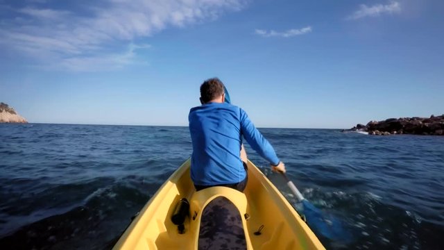 POV of passenger or sports activity partner from kayak in the middle of blue choppy water, sitting in the middle of yellow adventure kayak boat and paddeling together with a man in blue active wear