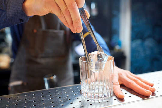 Bartender Adding Ice Cube Into Glass At Bar