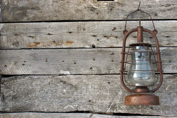Old kerosene lamp hanging on a rustic wooden wall of a barn, retro background texture