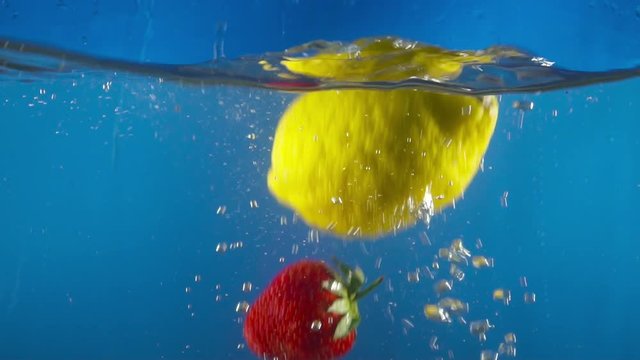 Closeup of fruits falling into water on the blue backgrond slow motion