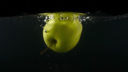 Closeup of green apple falling into water on the black backgrond slow motion - Powered by Adobe